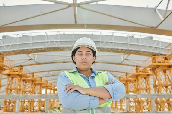 A Woman Wearing Safety Helmet and Vest Standing Near the Steel Structure