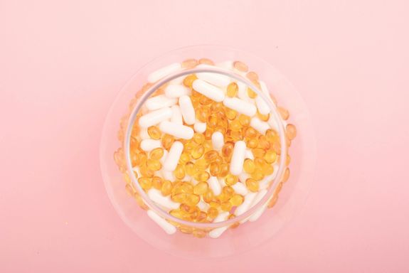 Top view of glass bowl filled with many capsules and pills for curing disease on pink background