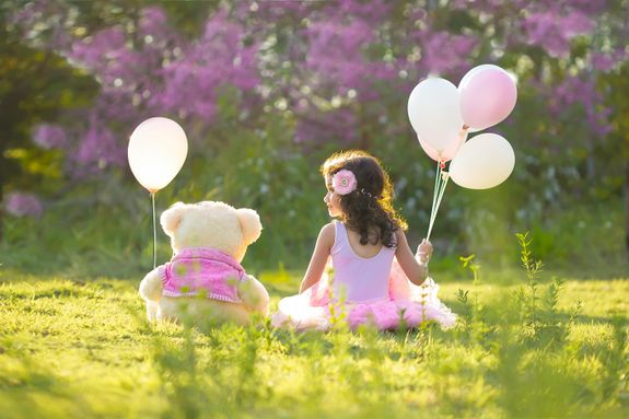 Little Girl Sitting with Her Teddy Bear and Holding Balloons 