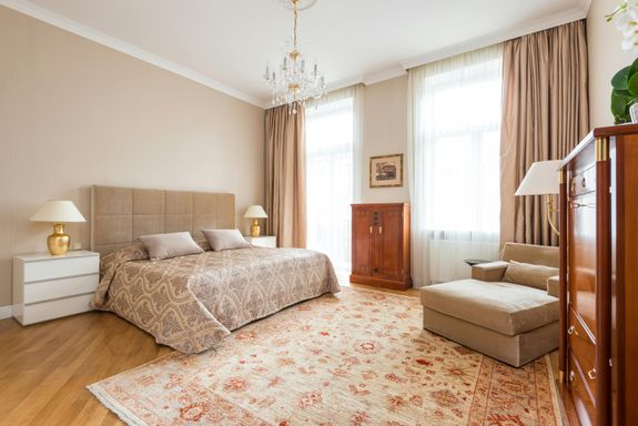 Classic interior bedroom furnished with bed near lamps on bedsides and armchair near wooden old fashioned dresser and cupboard