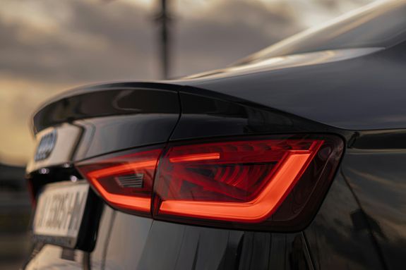 Close-up of a sleek black car's taillight with glowing red light during sunset, emphasizing design.