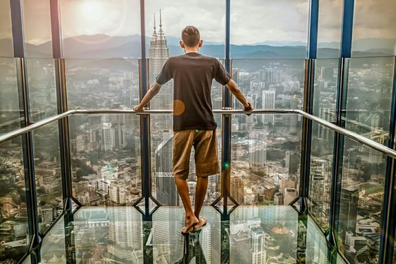 Man in Black T-shirt Looking Out of Glass Windows during Sunset