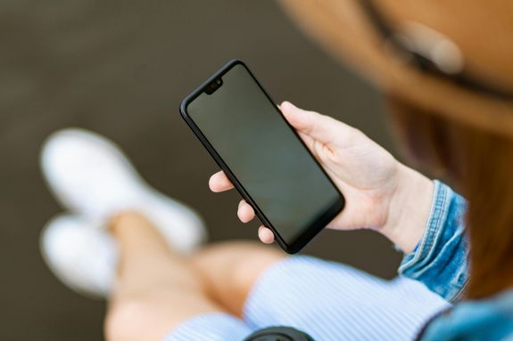 Close-up of a woman holding a smartphone, sitting outdoors in casual attire, focusing on screen.