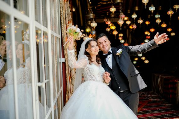 A bride and groom pose for a photo in front of a window