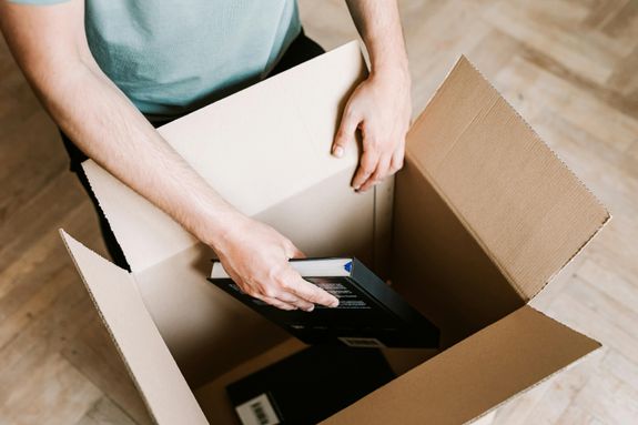Crop man packing books in carton box