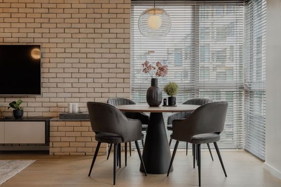 White table with lamp and chair under shelf with mirror near window decorated with pink curtains