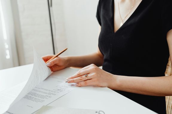 Woman with manicured nails examining documents at a desk, emphasizing detail and professionalism.