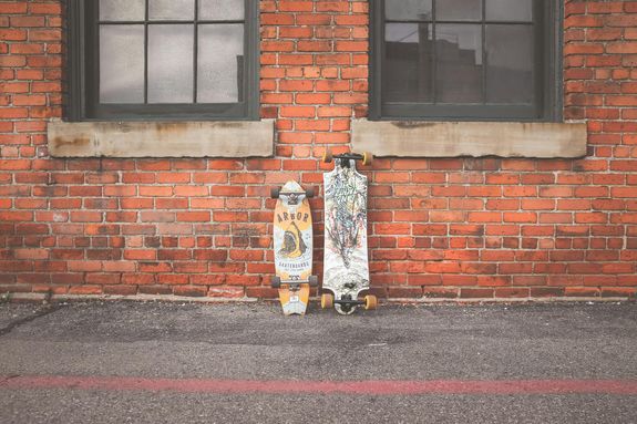 Two White and Brown Longboard Leaning on Brown Bricks Wall
