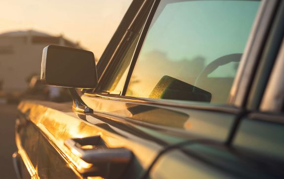 Close-up of a car side window and mirror reflecting sunset light, capturing a warm and peaceful moment.
