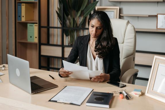 Business woman focused on paperwork at office desk, reviewing documents.