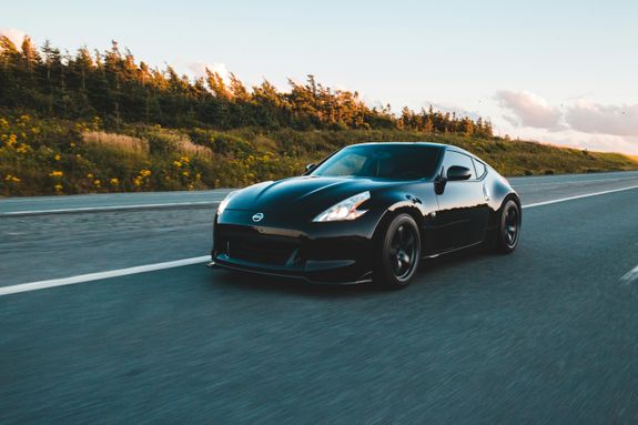 Modern luxury new automobile riding on asphalt road near bushy green forest with glade and flowers