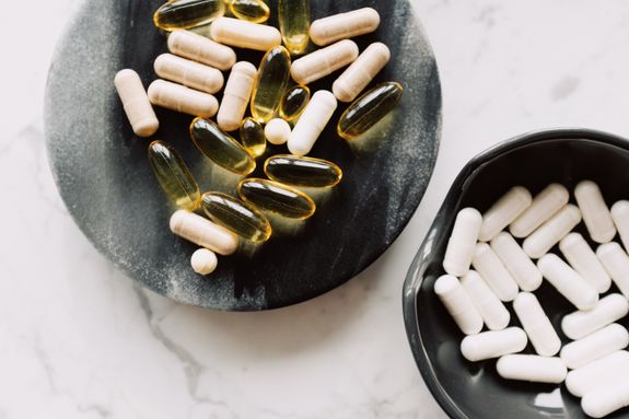 Vitamin capsules on black stone stand with pills in black bowl aside on table