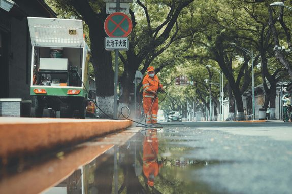 Man in Orange Jacket and Pants Standing on Road Using a Power Spray