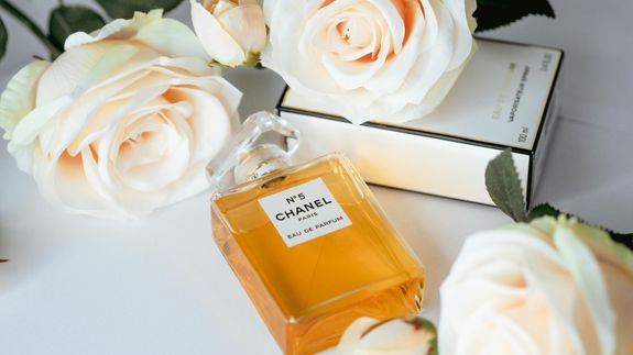 A Bottle of Chanel No 5 Perfume Lying on a White Surface with Flowers 