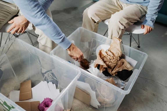 Close-up of hands sorting recyclable materials in clear plastic boxes indoors.