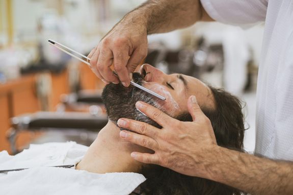 A Person Shaving a Man's Beard While Lying Down