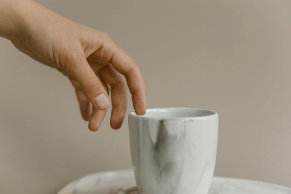 Close-Up Photo of a Person's Hand Touching a Ceramic Cup