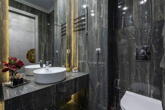 Interior of contemporary bathroom with black tiled walls and sink at mirror with flowers placed near modern bidet at home