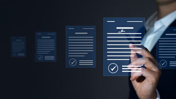 A Person in Black Suit Holding a Pen Near the Documents on the Table