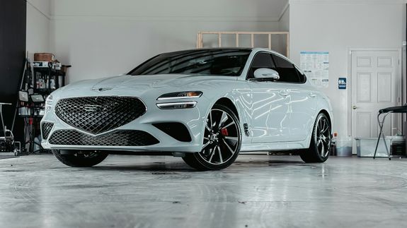 Detailed view of a sleek red sports car headlight with water droplets enhancing its glossy finish.