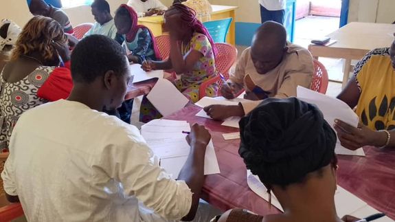A diverse group of coworkers discuss strategies around a laptop in a bright office space.