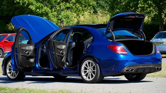 Close-up of a sleek black car's taillight with glowing red light during sunset, emphasizing design.