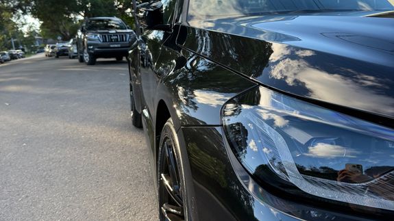 Polished reflecting surface of black modern car hood with glossy headlight on street