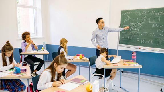 Side view full length young focused female in casual clothes browsing modern laptop and writing down notes while sitting on floor in cozy modern apartment
