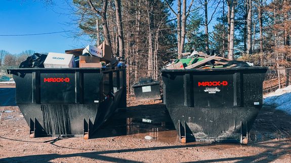 A close-up photograph of a black plastic garbage bag against a plain concrete wall, highlighting waste management.